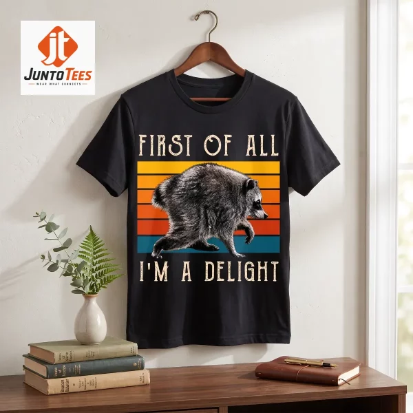 A charcoal black cotton t-shirt with a vintage sunset raccoon illustration displayed on a wooden surface.