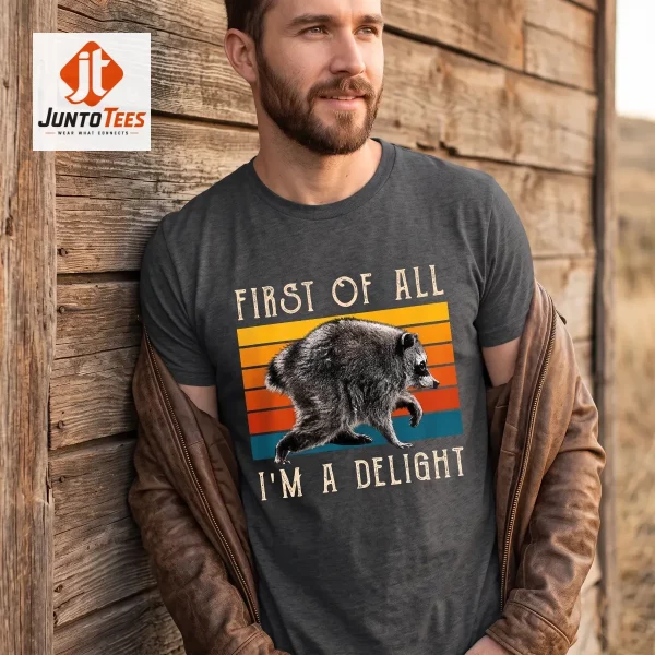 A charcoal black cotton t-shirt with a vintage sunset raccoon illustration displayed on a wooden surface. (Detail view #3)