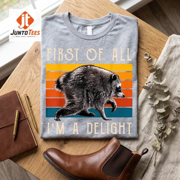 A charcoal black cotton t-shirt with a vintage sunset raccoon illustration displayed on a wooden surface. (Detail view #4)
