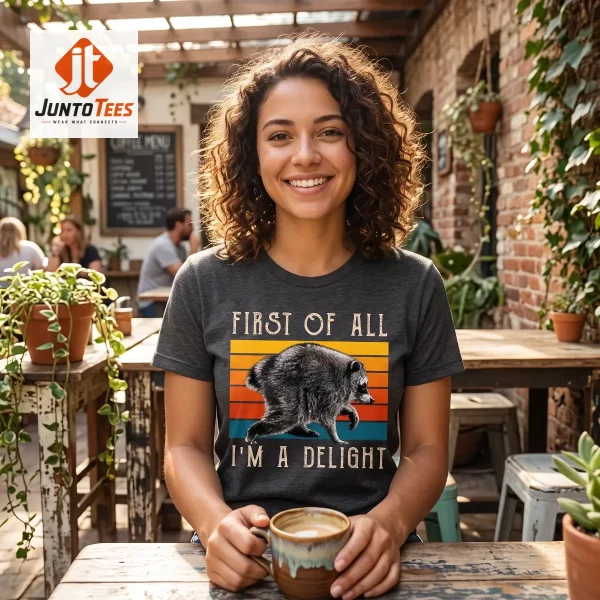 A charcoal black cotton t-shirt with a vintage sunset raccoon illustration displayed on a wooden surface. (Detail view #6)