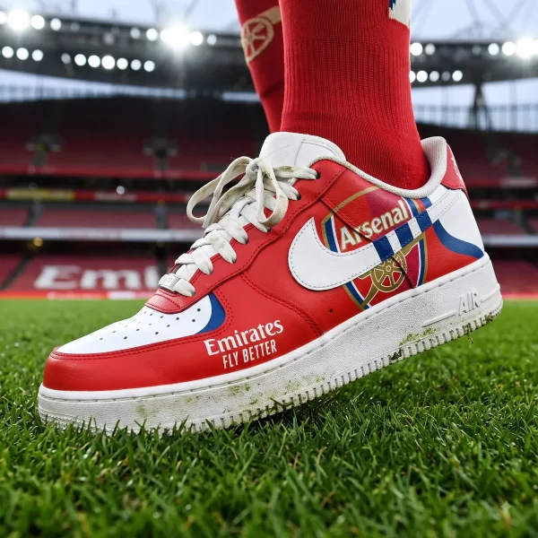 Side profile of Arsenal FC custom Nike Air Force 1 sneaker with Emirates Fly Better branding on a stadium pitch.