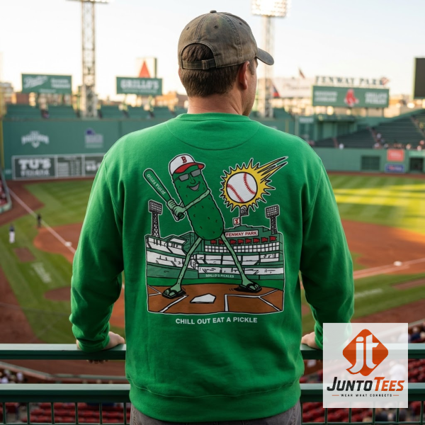 Boston Red Sox x Grillo's Pickles Crewneck Sweatshirt 2026 Fenway Park 1 Back view of a vibrant green Boston Red Sox x Grillo's Pickles crewneck sweatshirt, showcasing a detailed cartoon graphic of a pickle character in a baseball uniform, batting a baseball with Fenway Park in the background, laid flat on a rustic wooden surface.